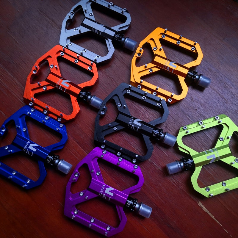 NEXT GEN ENZO ultra-light flat foot mountain bike pedals in titanium, orange, blue, gold, black, purple and green colours.